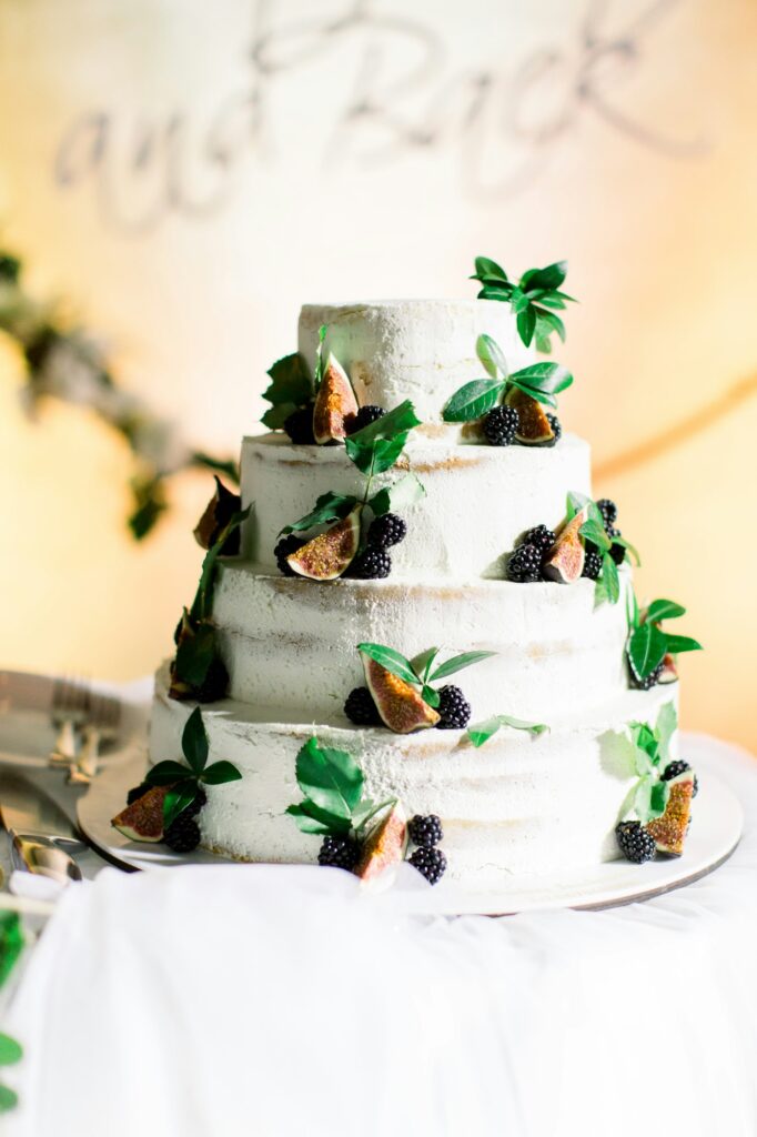 Naked wedding cake. White four-tiered wedding rustic cake with berries and figs and greenery, on the